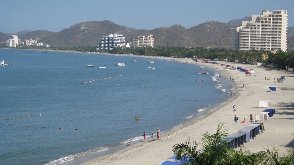 Playa de arena y bahía de Santa Marta con edificios y montañas al fondo